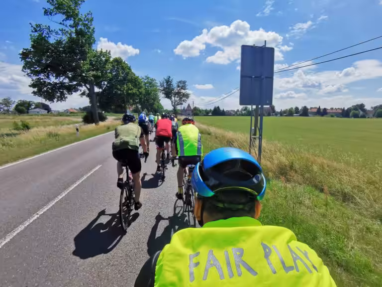 Radfahrergruppe von hinten auf einer Landstraße, ein Fahrer trägt eine Warnweste