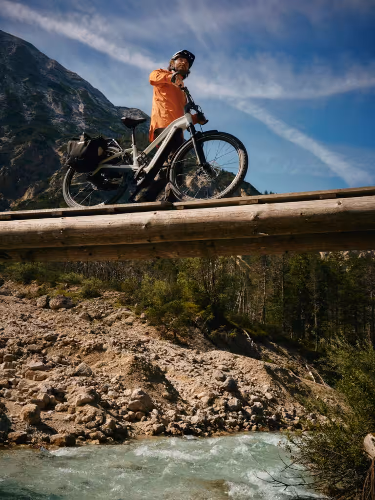 Person mit Trekking-E-Bike auf einer Brücke über einem Fluss